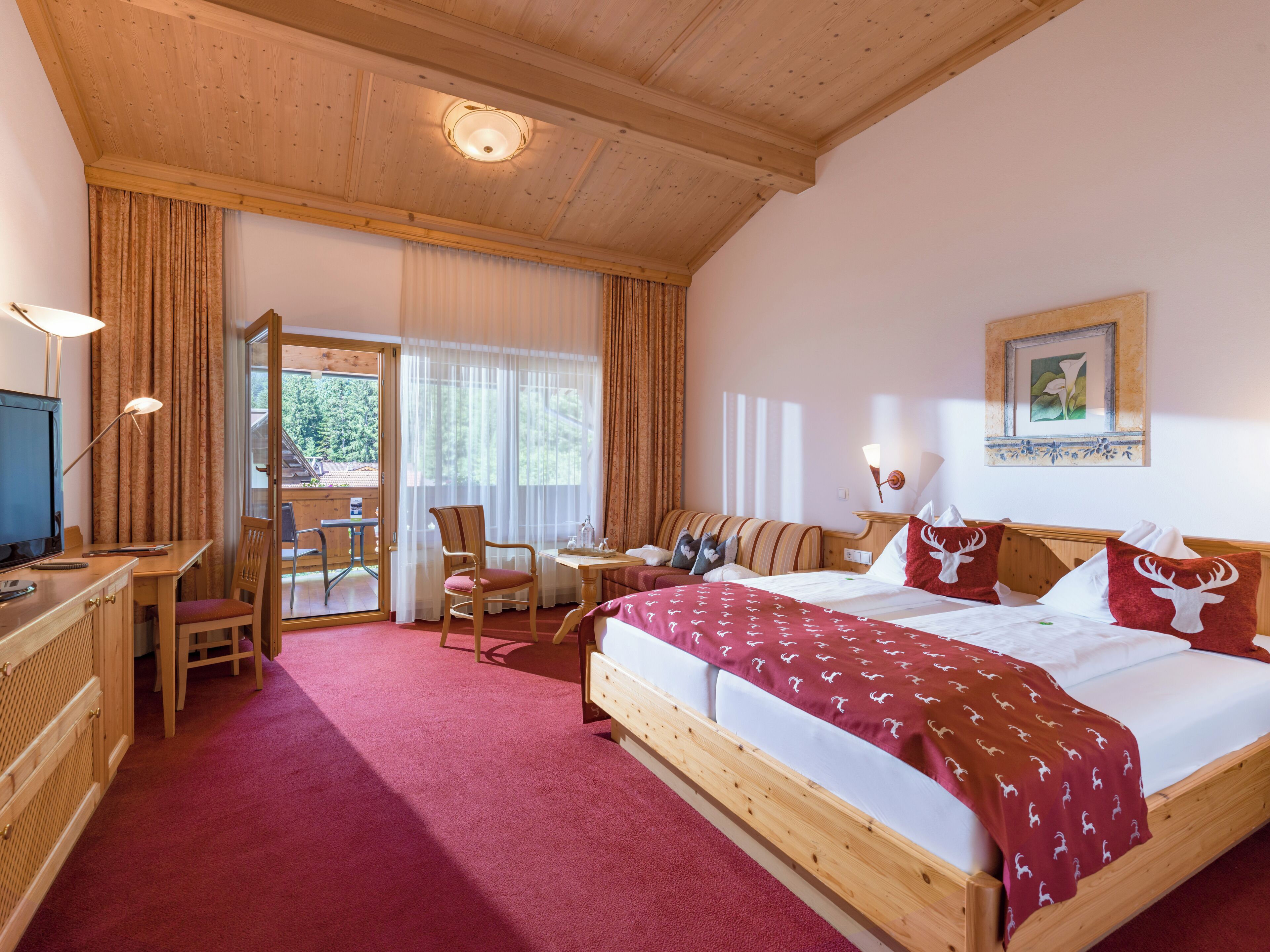 A hotel room with a wooden bed, a desk with a computer, a chair, a small table, and a window with curtains.