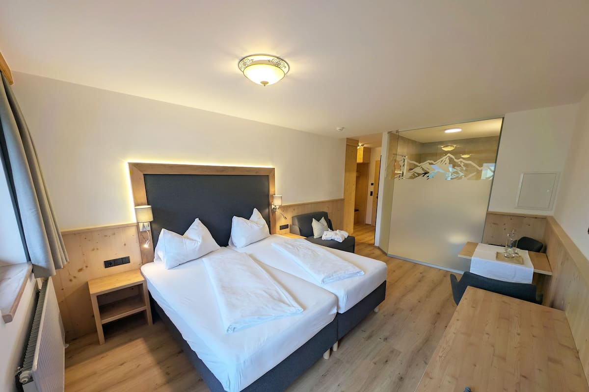 A hotel room with two beds, a wooden floor, a large mirror, and a small desk with a chair.
