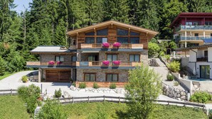 Un immeuble à plusieurs étages, doté d’une façade en pierre, de balcons en bois et, au loin, d’un télésiège.