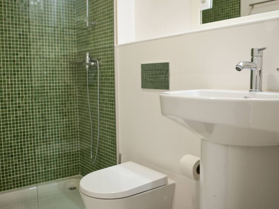 A bathroom with a shower, toilet, sink, and a trash can.