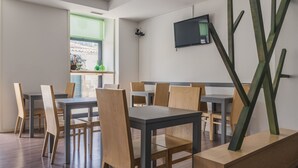 Un comedor moderno con varias mesas y sillas, un televisor de pantalla plana montado en la pared y una ventana con vistas al exterior.