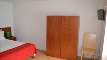Une chambre à coucher avec un lit, une armoire en bois, une chaise en bois et un téléviseur fixé au mur.