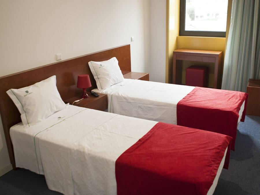 A hotel room with two single beds, a small table, a lamp, and a window with curtains.