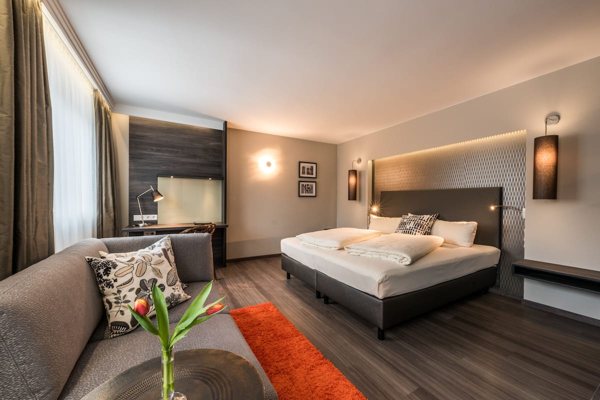 Una habitación de hotel moderna con una cama grande, un sofá, un escritorio y una mesita de noche.