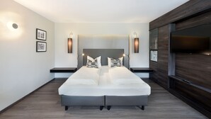 A modern bedroom with a large bed, two bedside tables, wall-mounted lights, and a dark wood paneling on the right side. - Hotel Säntis (Munich)