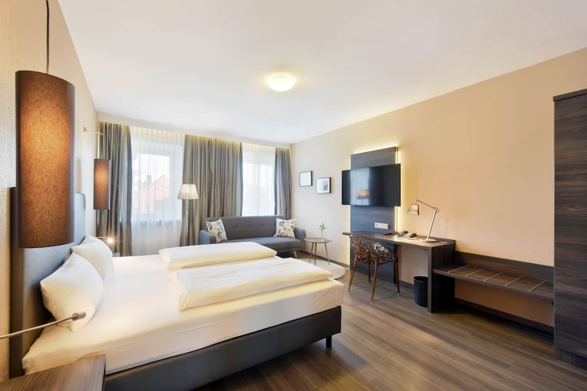 Una habitación de hotel moderna con una cama grande, un escritorio, un televisor y un área de descanso.