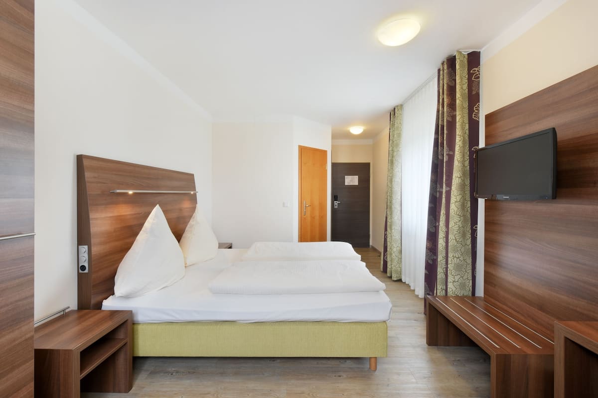 Habitación de hotel con una cama grande, un televisor montado en la pared y un cabecero de madera.