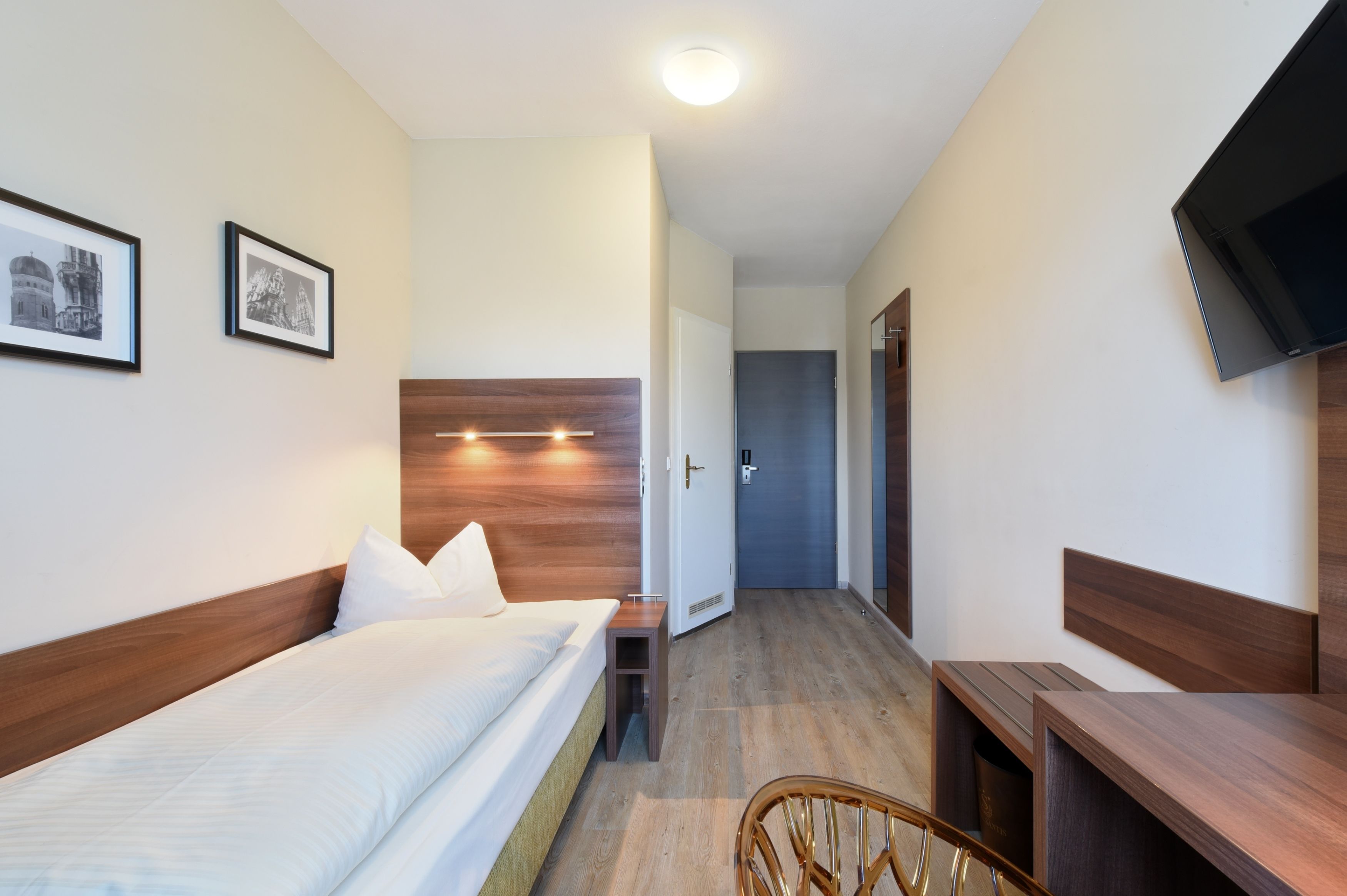 A hotel room with a bed, bedside table, chair, and a television on the wall.