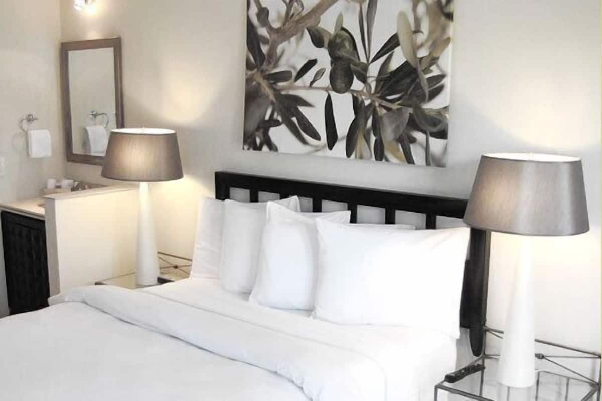 Una camera d'albergo con un letto, due abat-jour, uno specchio e un bagno visibile attraverso una porta aperta.