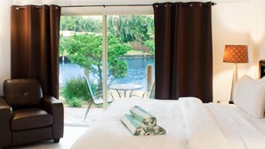 A hotel room with a bed, a chair, a table, and a view of a pool and greenery.