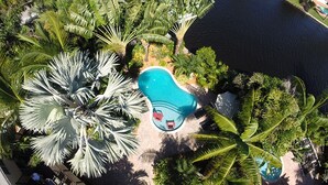 An aerial view of a resort with a swimming pool surrounded by palm trees and a body of water.