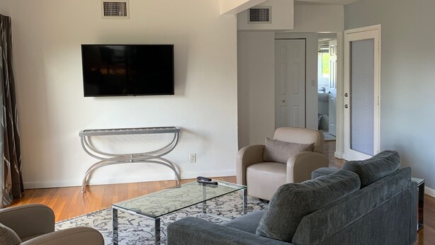 A modern living room with a grey sofa, a glass coffee table, and a white armchair.