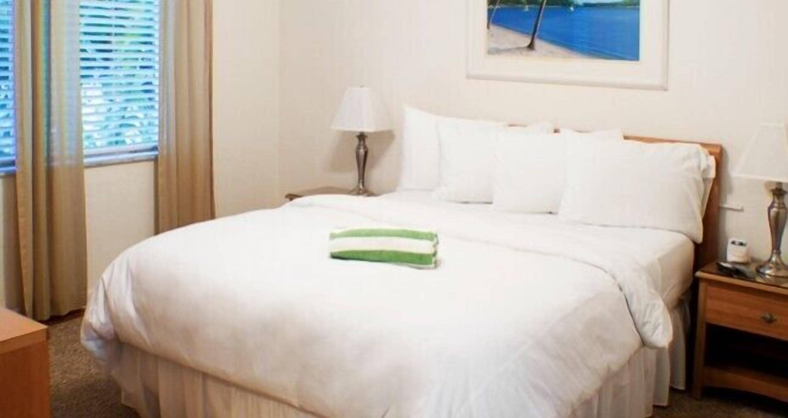 A hotel room with a bed, a nightstand, a lamp, and a painting of a beach scene.