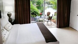 A bedroom with a large bed, a view of a garden through a sliding glass door, and a small table with chairs outside.