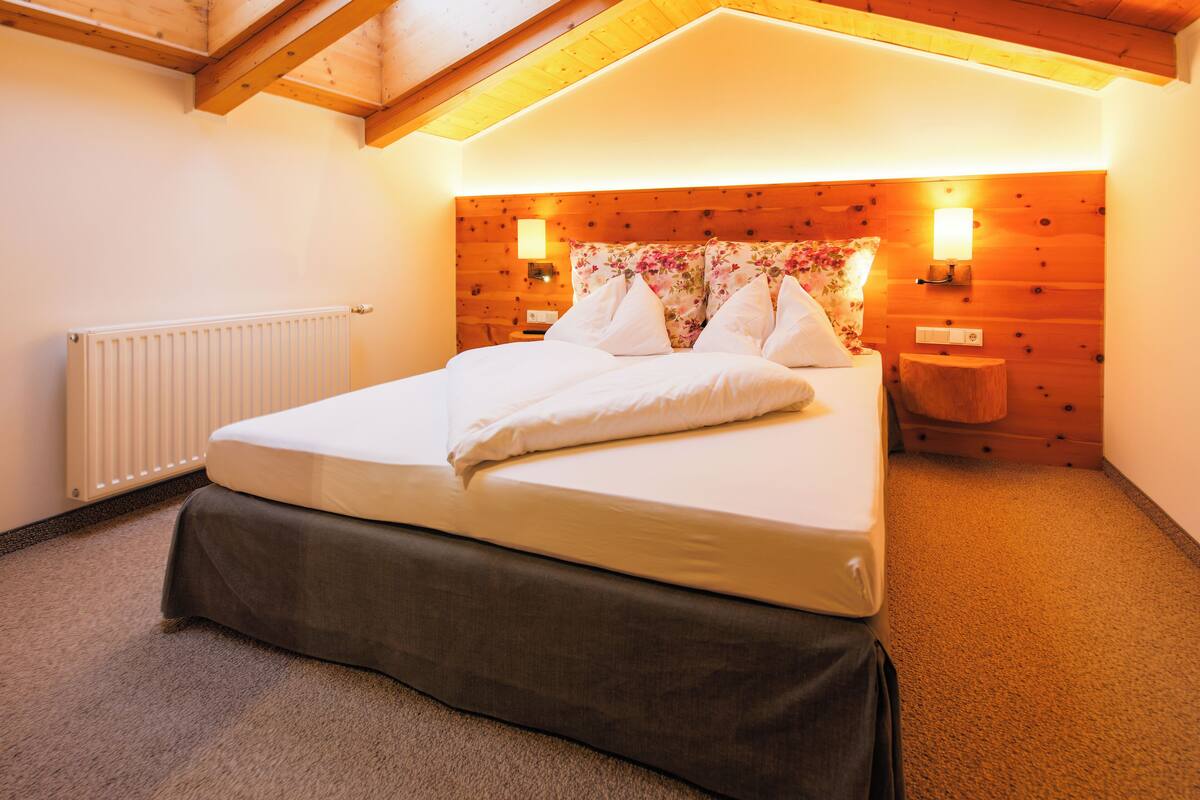 A bedroom with a bed, wooden headboard, two bedside lamps, and a radiator.