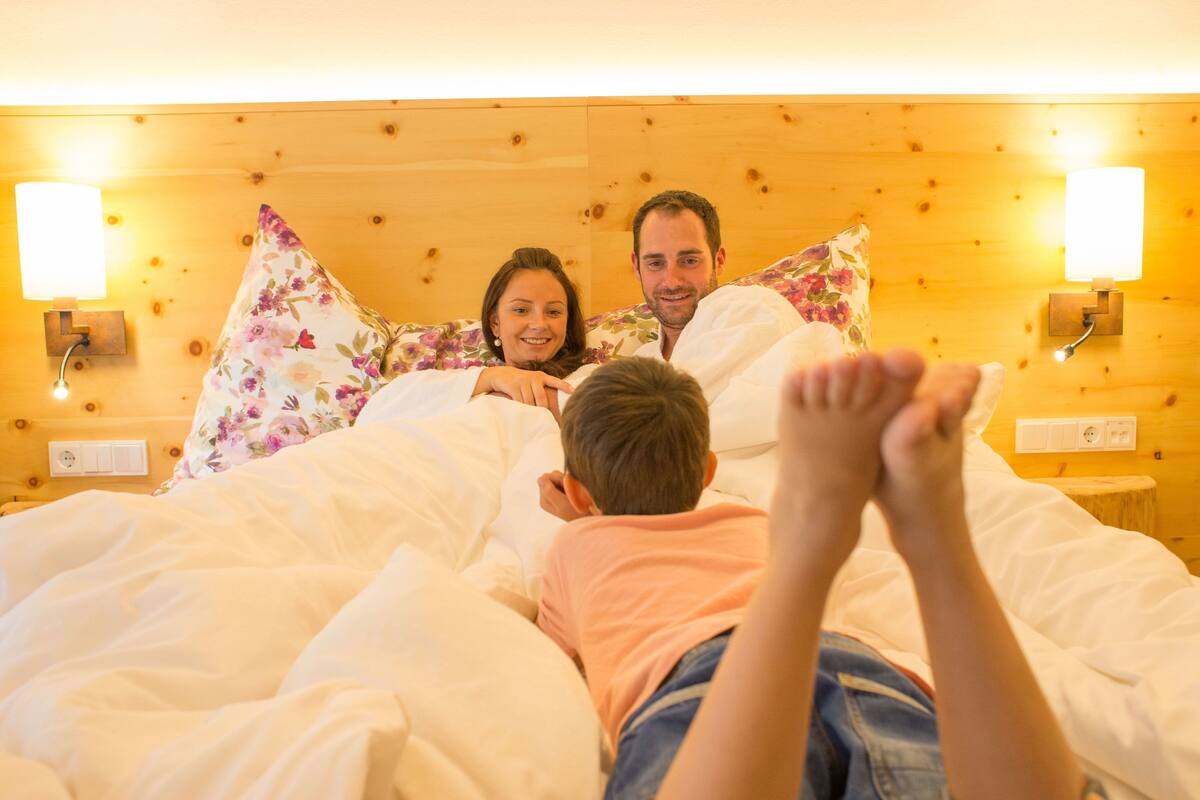 A family in a cozy room with wooden paneling and two wall-mounted lamps.