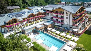 A hotel with multiple balconies adorned with flowers, a swimming pool, and solar panels on the roofs.