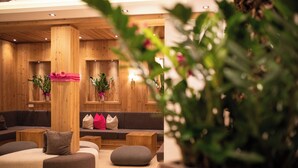 A modern lounge area with wooden walls, cushioned seating, and decorative plants.