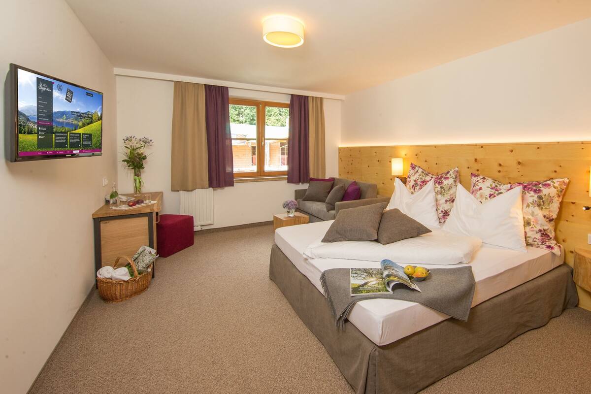 A hotel room with a bed, a sofa, a TV, and a wooden headboard.