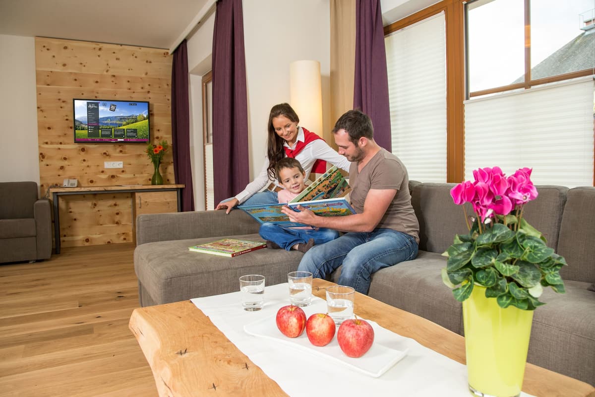 A living room with a wooden wall, a television, a sofa, a coffee table with apples and glasses, and a vase of flowers.