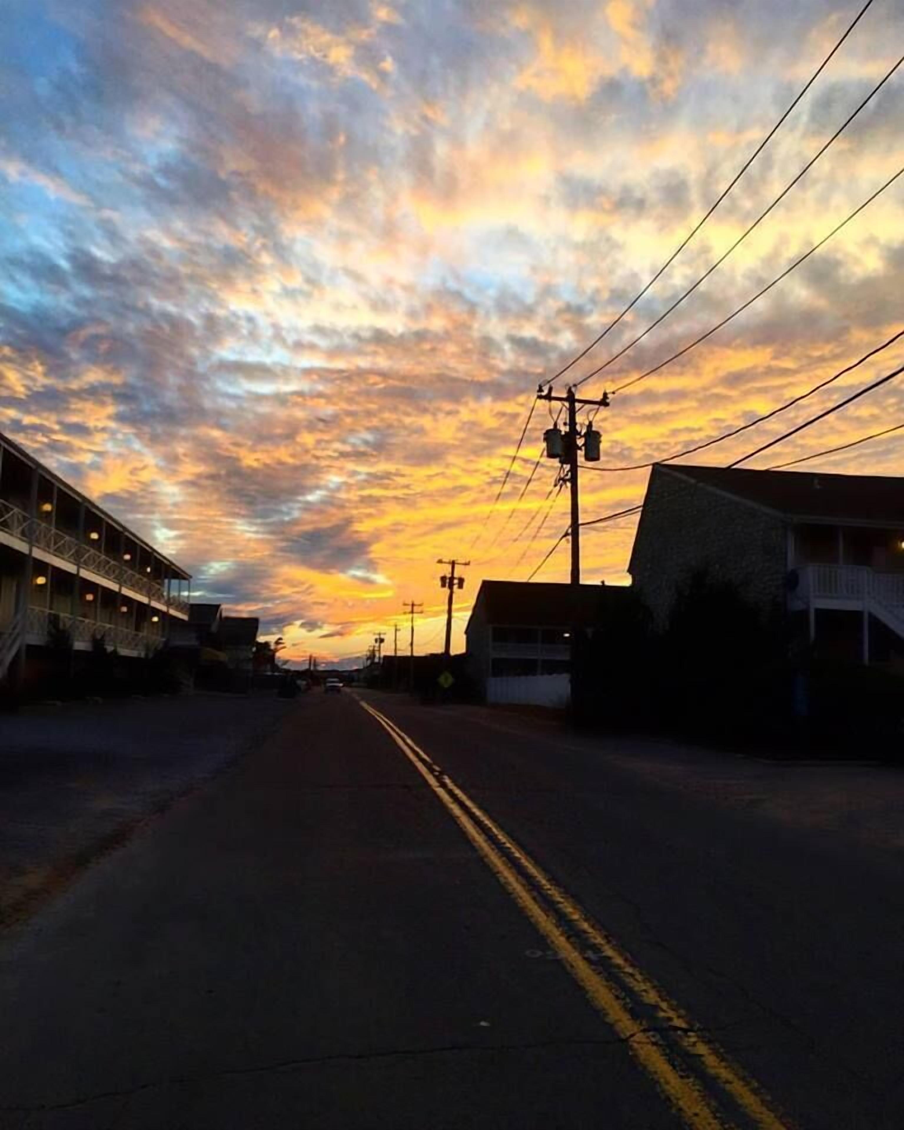 Una calle flanqueada por edificios, con líneas eléctricas sobre ella y un cielo al atardecer.