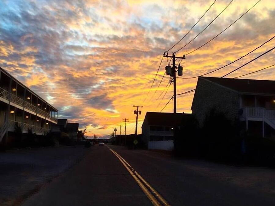 Una calle flanqueada por edificios, con líneas eléctricas sobre ella y un cielo al atardecer.