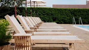 A row of wooden lounge chairs with white umbrellas, aligned along a poolside area with a hedge and a building in the background. - Daunt's Albatross Motel (Montauk)