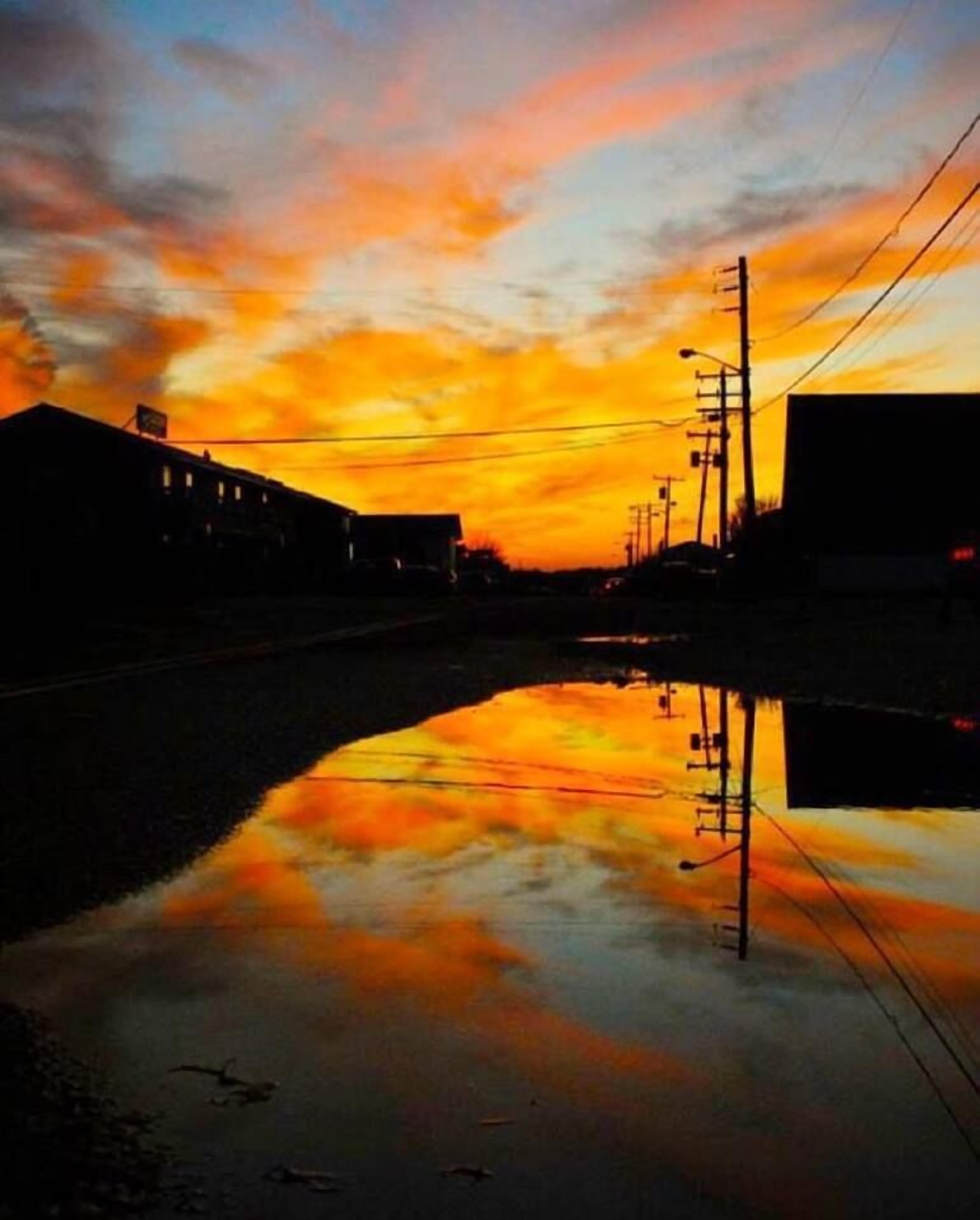 A sunset over a calm body of water reflecting buildings and power lines.