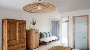 A bedroom with a wooden wardrobe, a bench, a large woven ceiling light, and a door. - Daunt's Albatross Motel (Montauk)