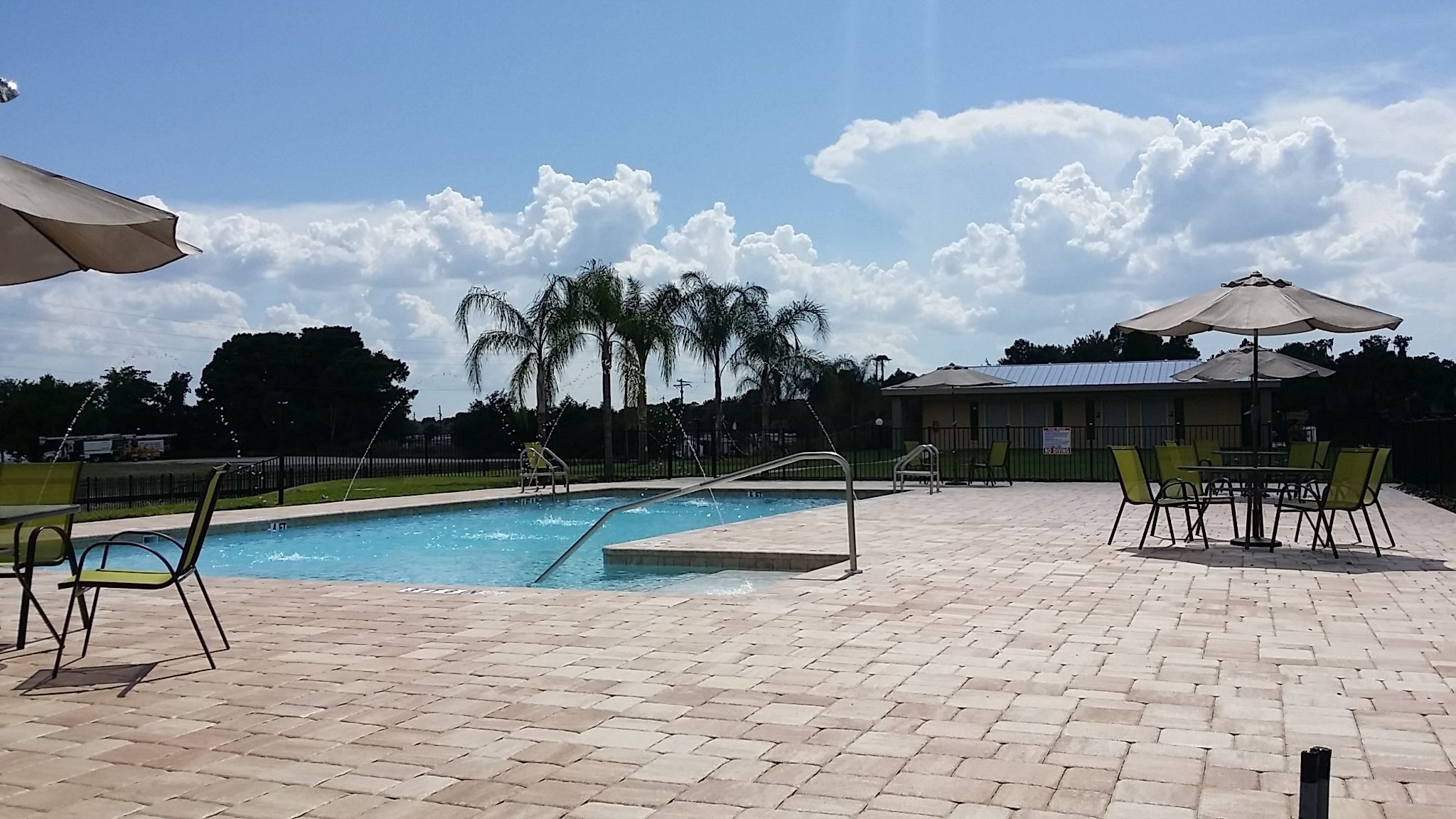 Une piscine avec une terrasse carrelée, entourée de chaises et de parasols, et un bâtiment en arrière-plan.