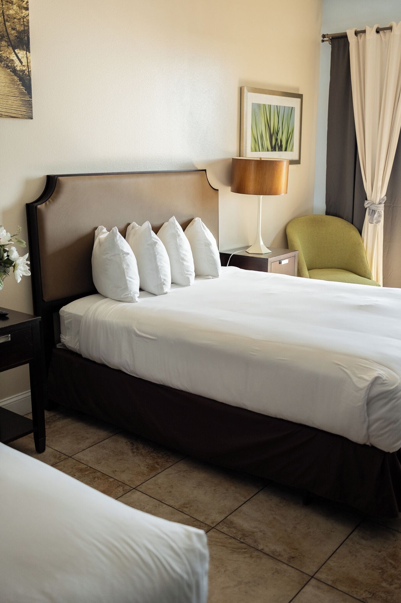 Habitación de hotel con una cama grande, una mesita de noche, una lámpara, una silla y un cuadro en la pared.