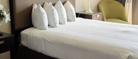 Habitación de hotel con una cama grande, una mesita de noche, una lámpara, una silla y un cuadro en la pared.