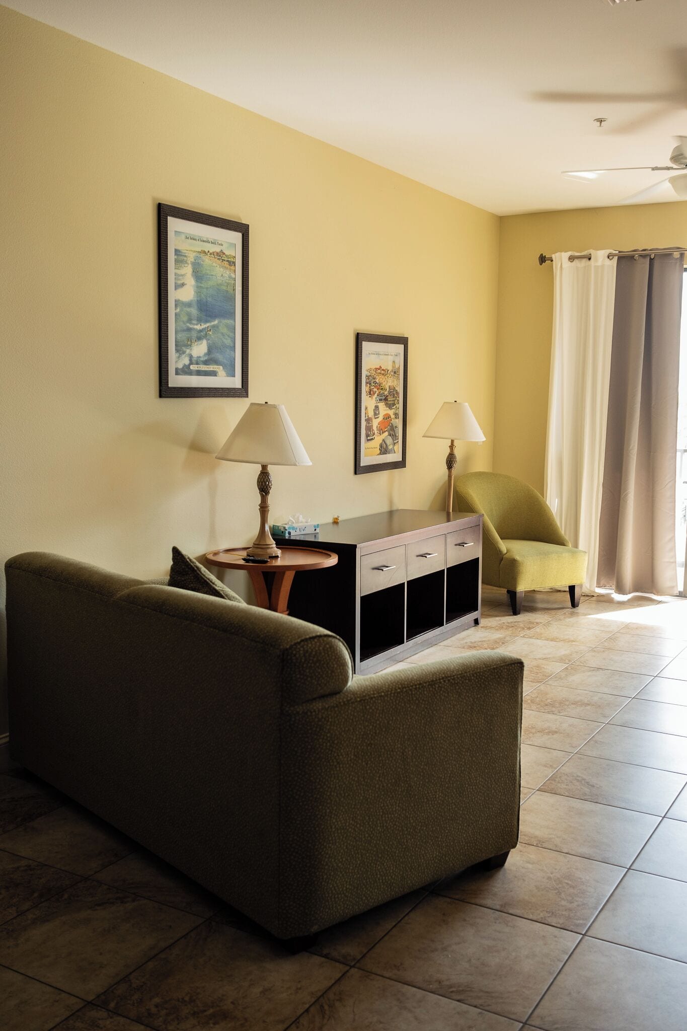 A living room with a sofa, a side table with a lamp, a cabinet, and two framed pictures on the wall.