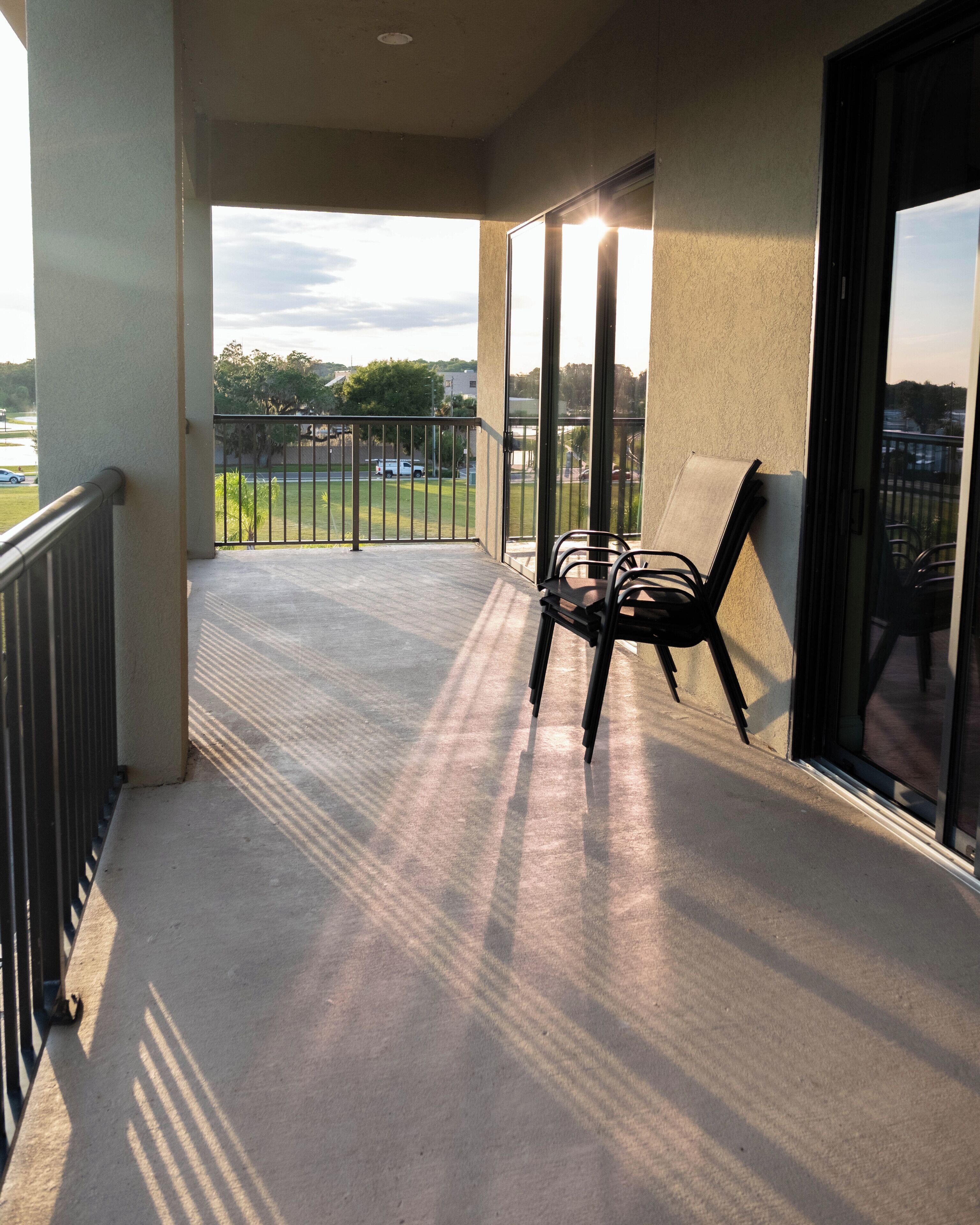 A balcony with a chair, a view of a parking lot, and a building in the background.