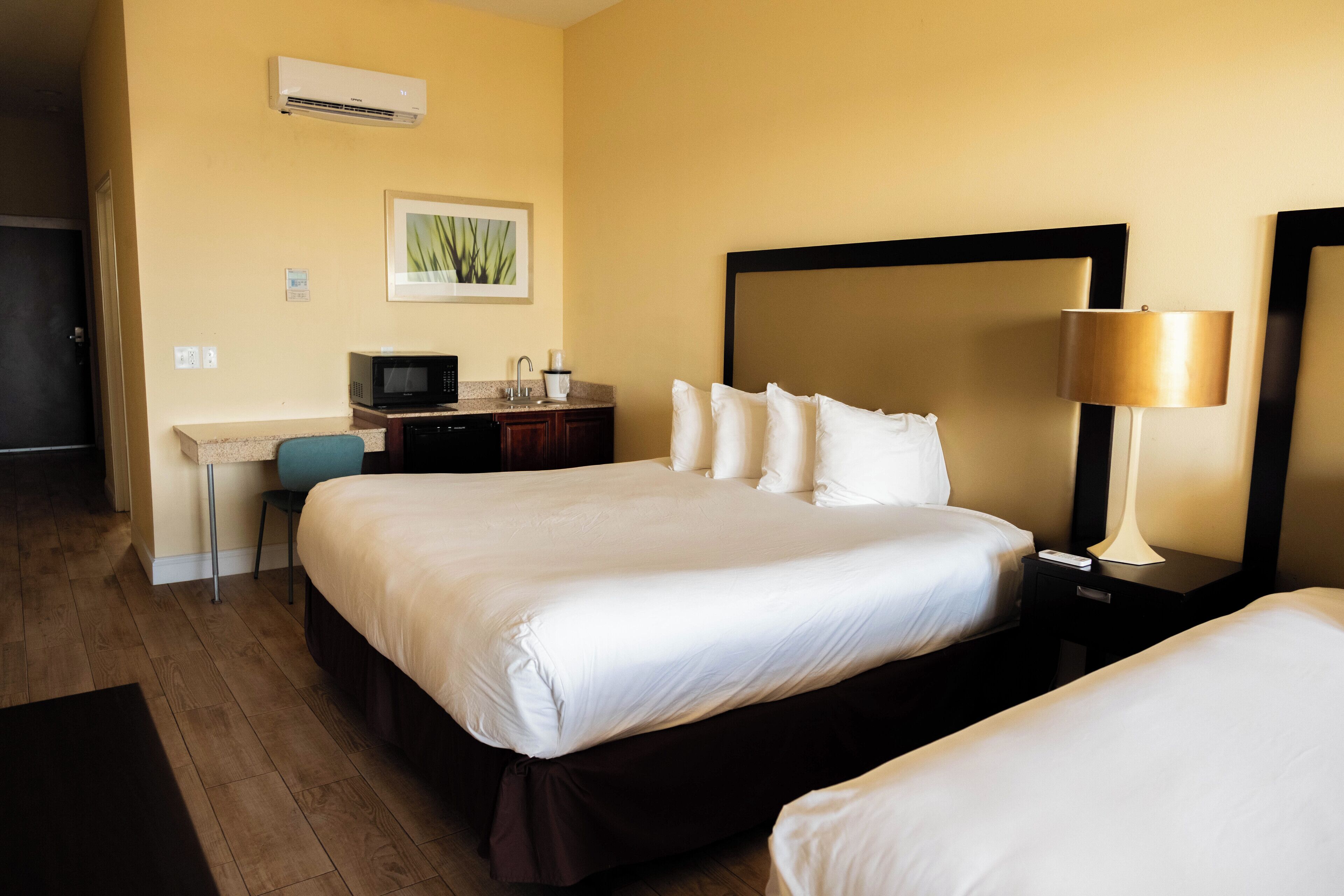 A hotel room with a large bed, a desk with a computer, a chair, and a lamp.