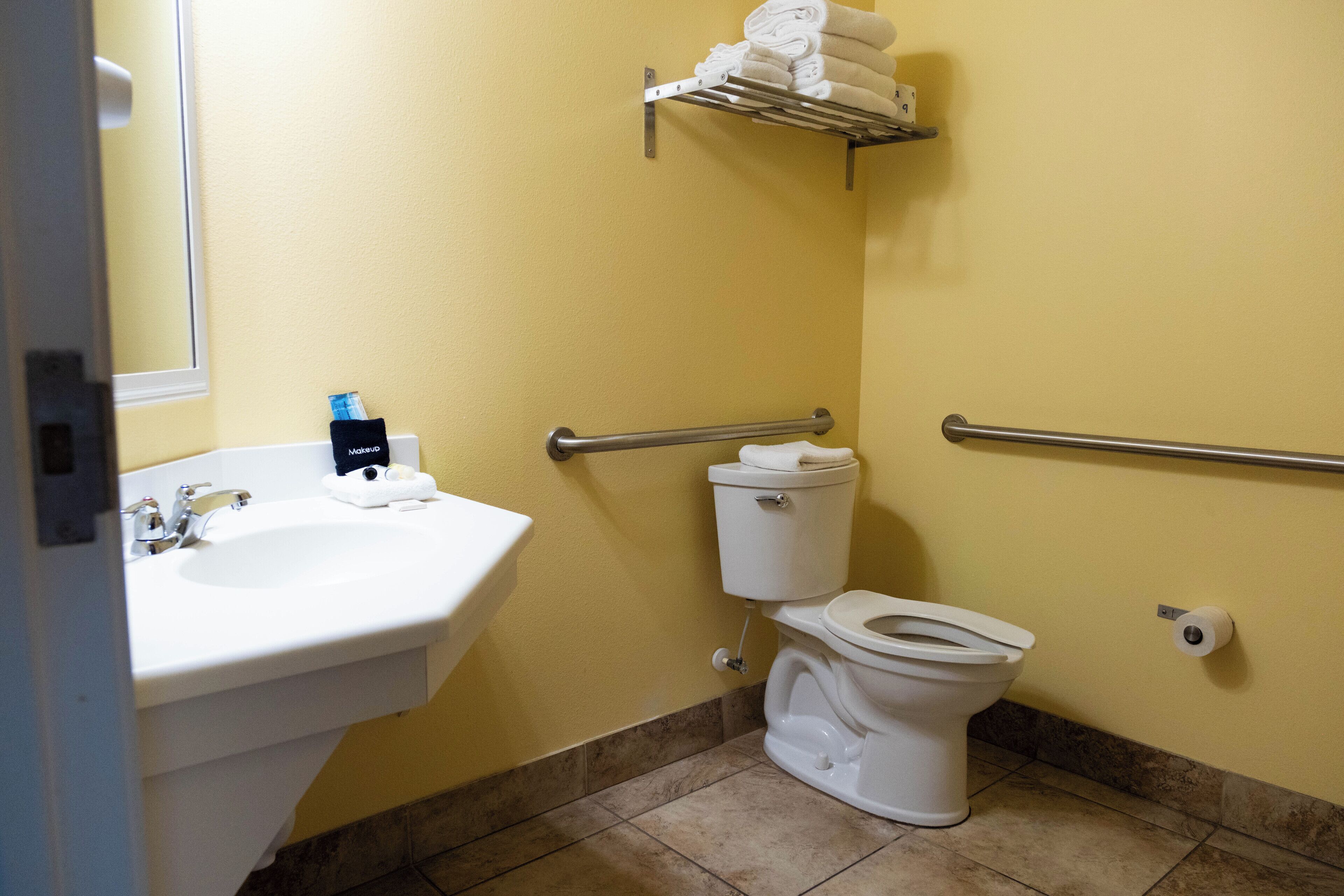 A bathroom with a sink, toilet, and handrails.