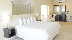 A hotel room with a large bed, a desk with chairs, a kitchenette, and a large painting on the wall. - The Citrus on the Lake (Tavares)