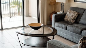 A modern living room with a grey sofa, a round coffee table with a bowl, and a view of the outdoors through a sliding glass door. - The Citrus on the Lake (Tavares)