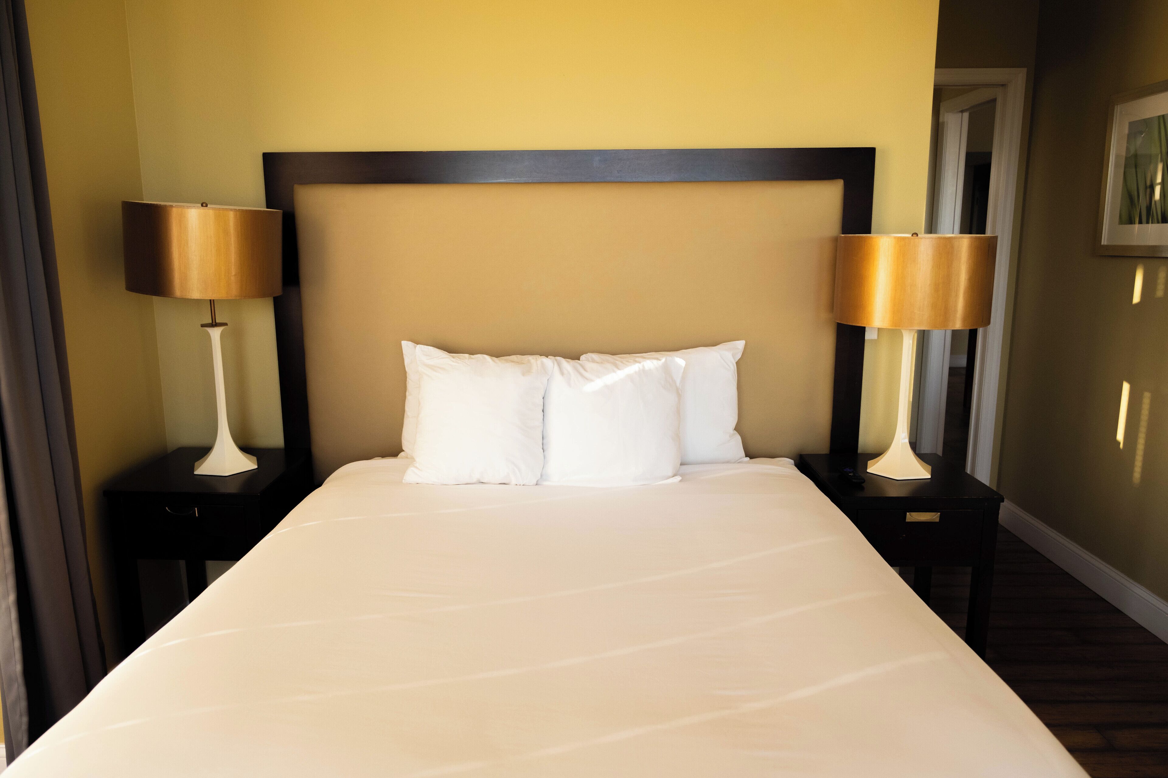 A neatly made bed with white linens, flanked by two bedside tables with lamps, in a room with a dark wooden headboard and light-colored walls.
