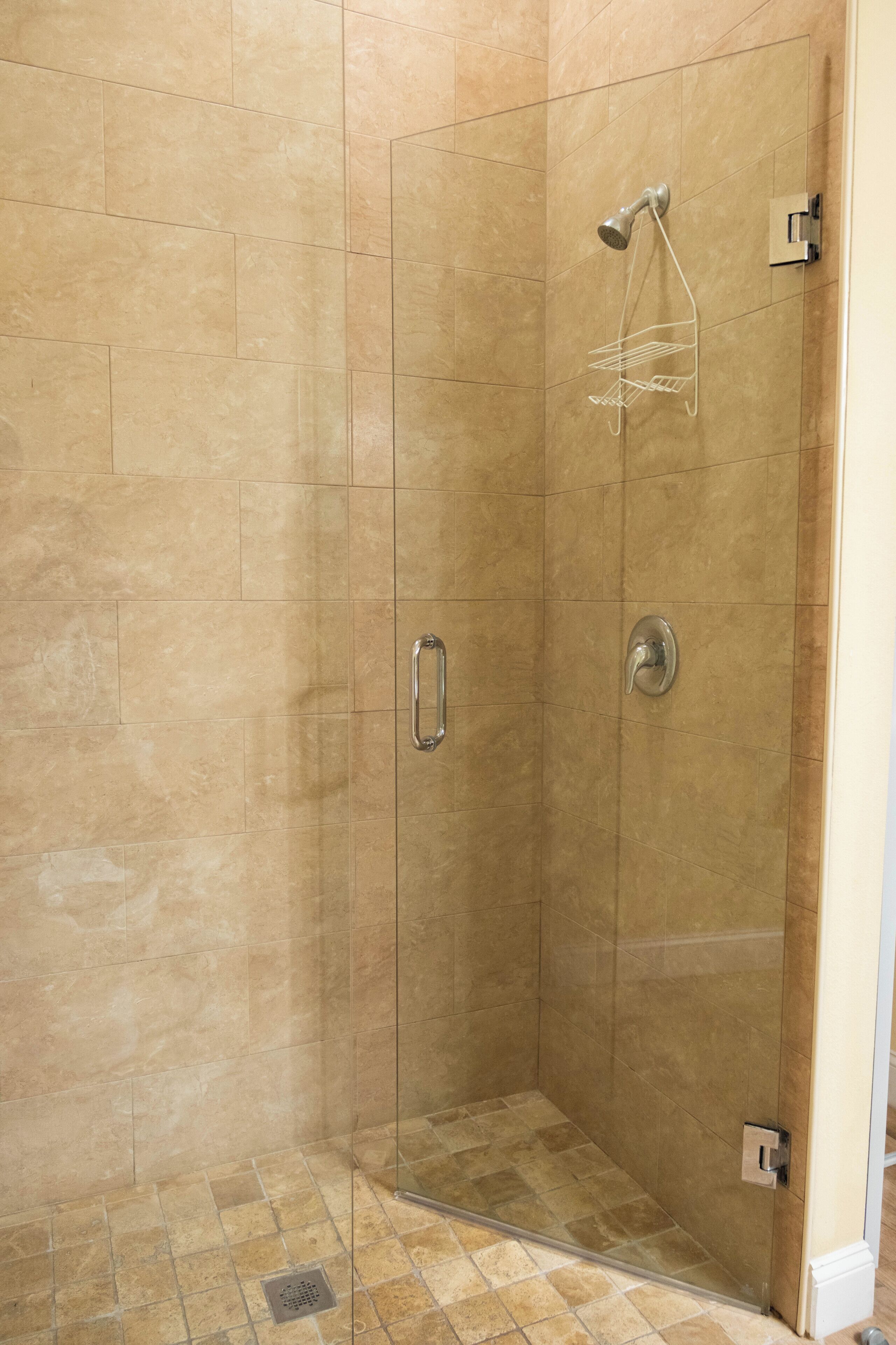 Ducha a pie con azulejos color beige, puerta de cristal y rociador.