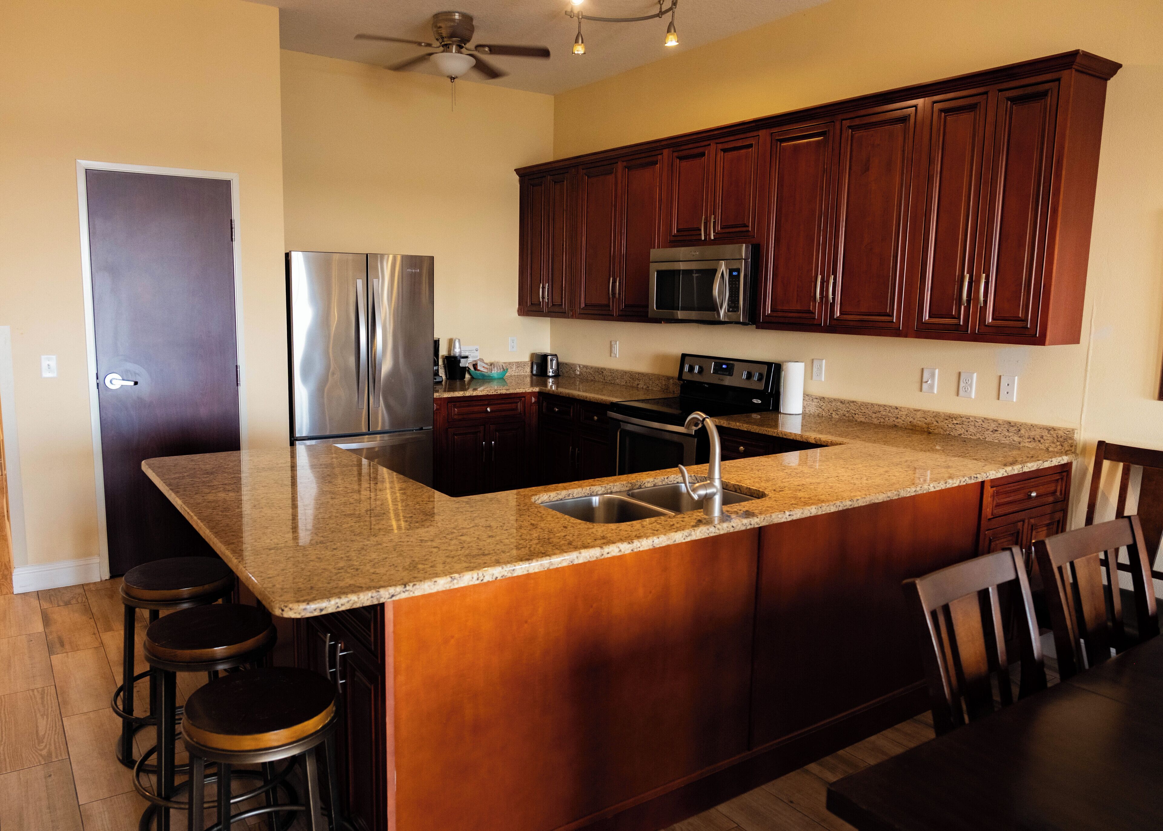 A kitchen with dark wooden cabinets, stainless steel appliances, granite countertops, and a ceiling fan.