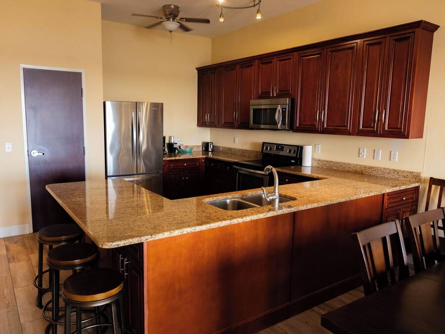 A kitchen with dark wooden cabinets, stainless steel appliances, granite countertops, and a ceiling fan.