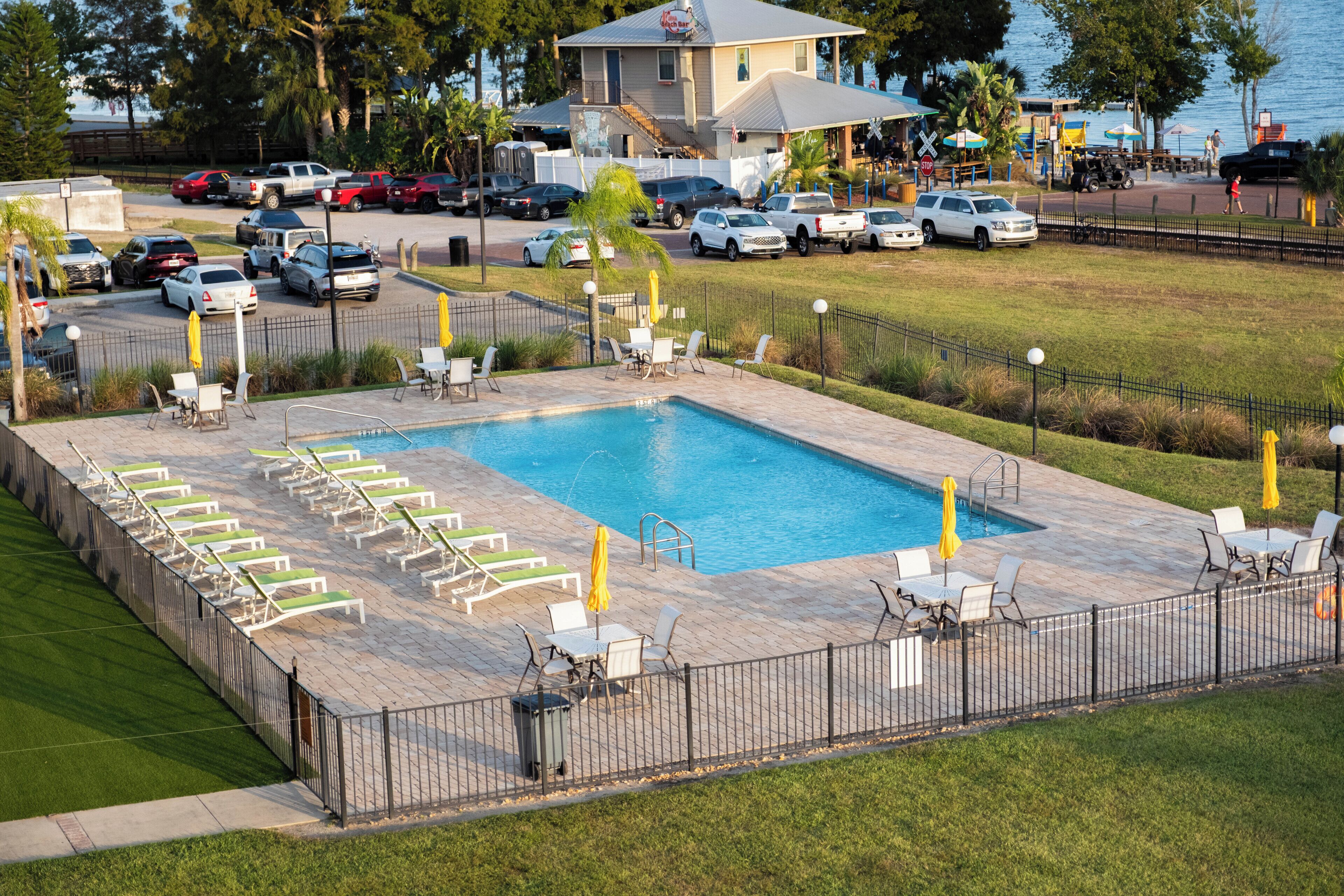 A swimming pool with lounge chairs and umbrellas, surrounded by a fence.