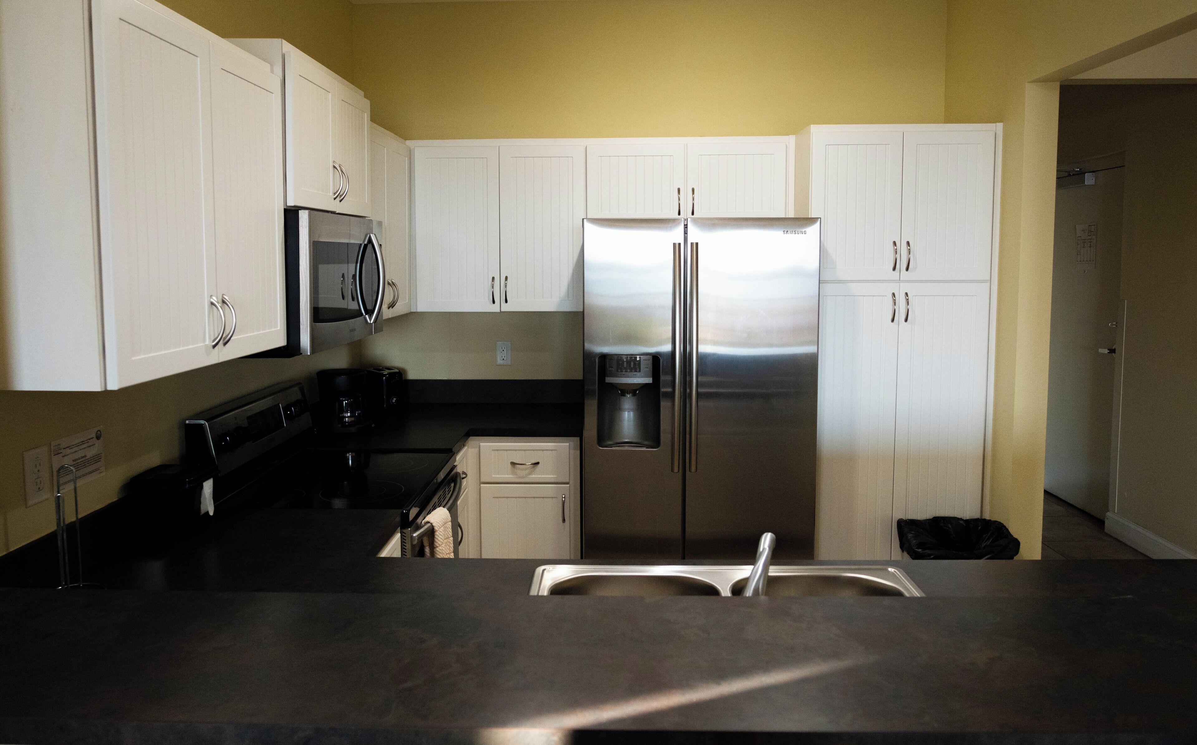 Una cocina con gabinetes blancos, un refrigerador de acero inoxidable, un microondas y una cafetera.