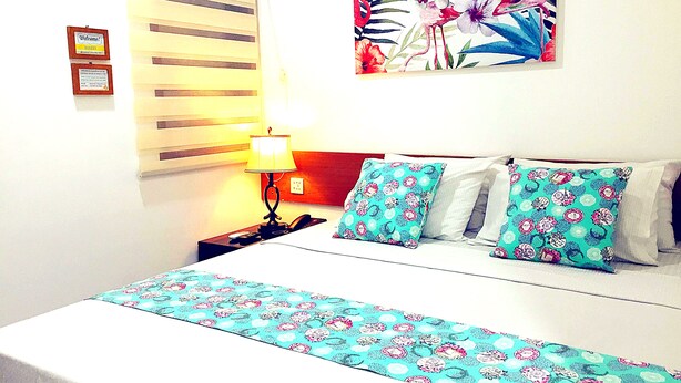 A hotel room with a bed, a nightstand, a lamp, and a floral artwork on the wall. - Sm Residence Pasteur (Bandung)