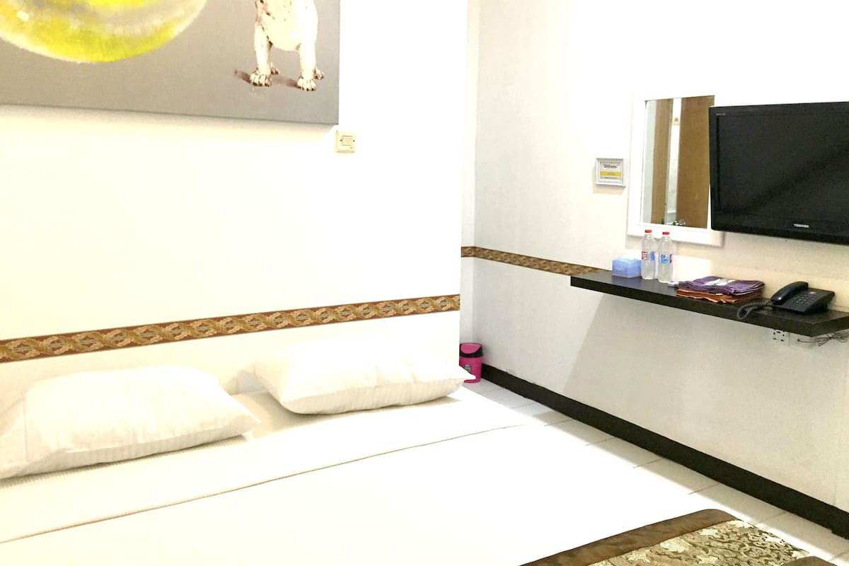 A hotel room with a bed, pillows, a TV, a shelf with toiletries, and a wall-mounted artwork.
