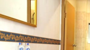 A bathroom with a mirror, a shelf with two bottles, and a door leading to another room. - Sm Residence Pasteur (Bandung)