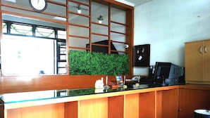 A reception area with a wooden counter, a clock, a green wall, and two pink stools. - Sm Residence Pasteur (Bandung)