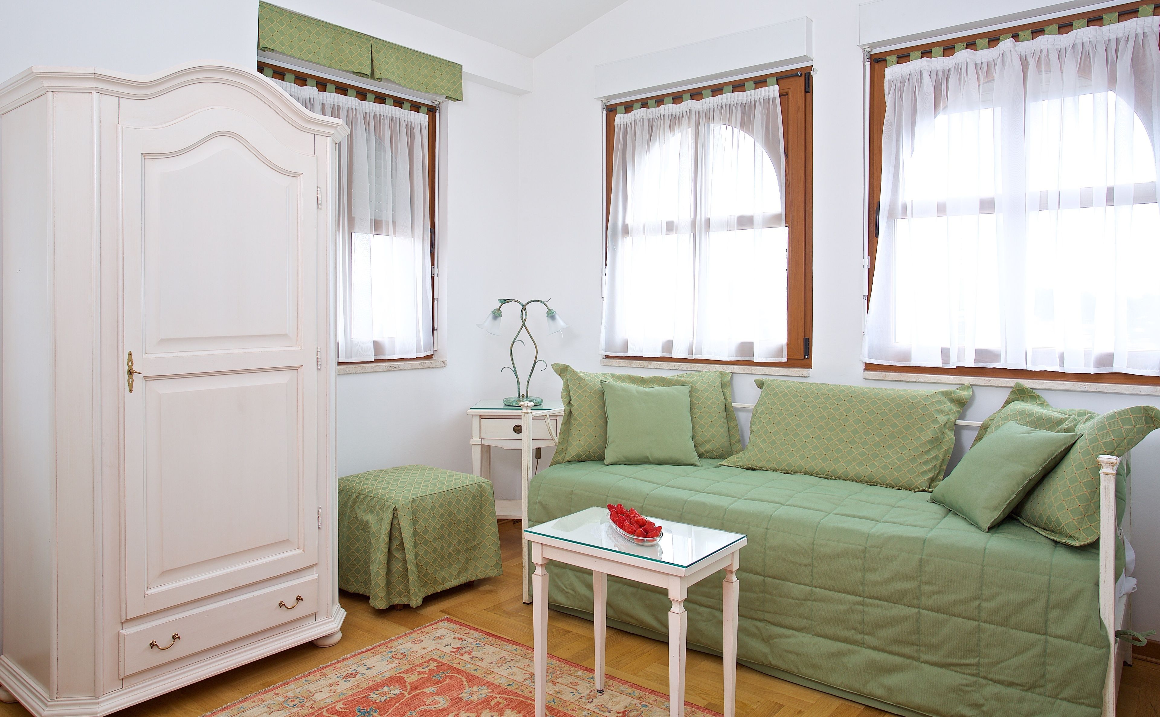 Una habitación con un sofá verde, un armario blanco, una mesita con un cuenco y una ventana con cortinas.