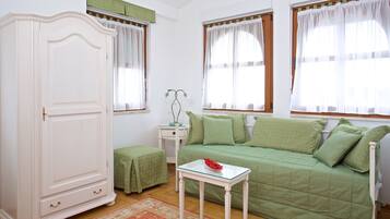 Una habitación con un sofá verde, un armario blanco, una mesita con un cuenco y una ventana con cortinas.